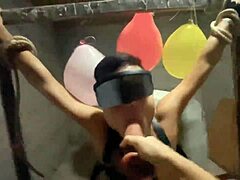 Junge weibliche dominante Herrin fesselt und verwöhnt unterwürfigen Mann oral im Keller mit Dildo