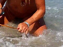 Зряла жена с разтегнати пиърсинг на зърната и множество пиърснги на путката на плажа
